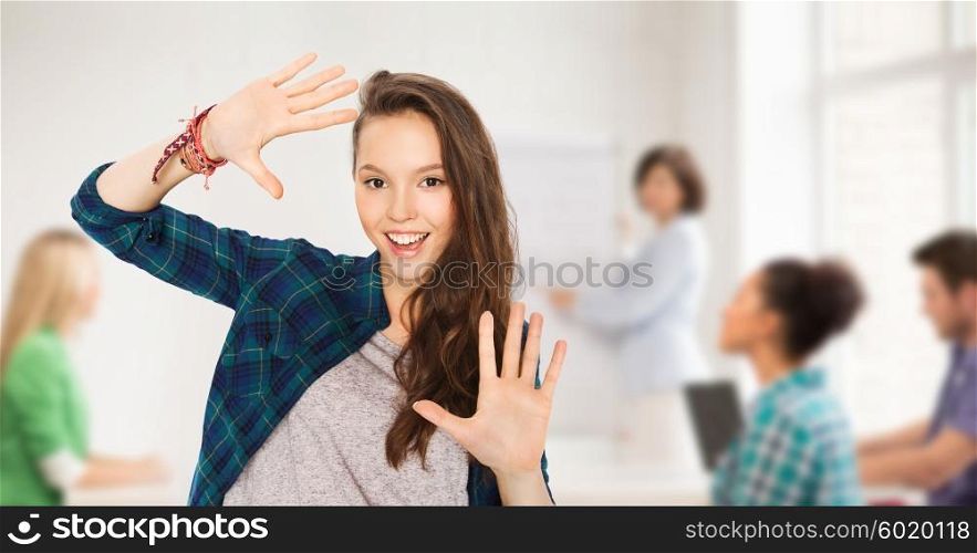 school, education, people and teens concept - happy smiling pretty teenage student girl showing hands over classroom background with teacher and classmates
