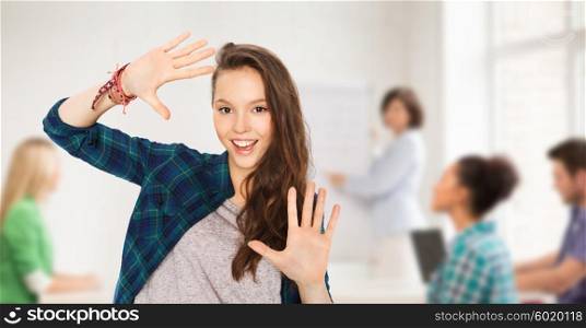 school, education, people and teens concept - happy smiling pretty teenage student girl showing hands over classroom background with teacher and classmates