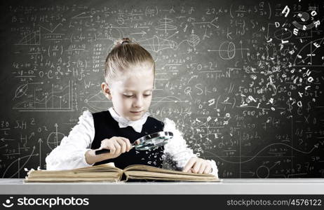 School education. Schoolgirl examining opened book with magnifying glass