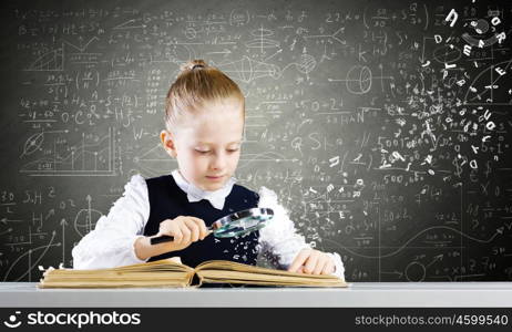 School education. Schoolgirl examining opened book with magnifying glass