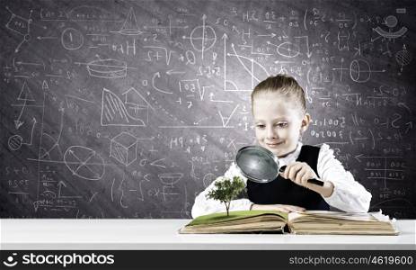 School education. Schoolgirl examining opened book with magnifying glass