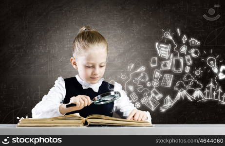 School education. Schoolgirl examining opened book with magnifying glass