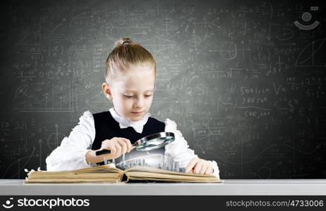 School education. Schoolgirl examining opened book with magnifying glass