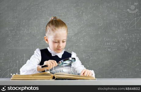 School education. Schoolgirl examining opened book with magnifying glass