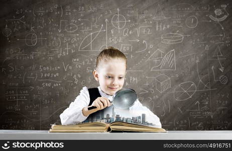 School education. Schoolgirl examining opened book with magnifying glass