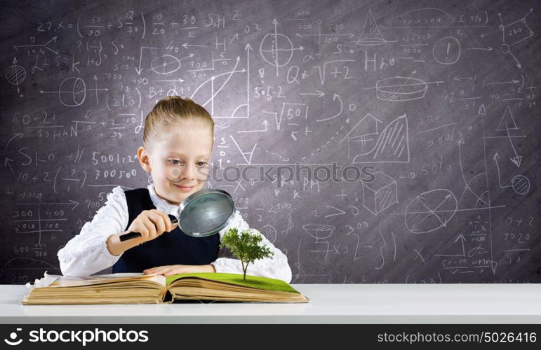 School education. Schoolgirl examining opened book with magnifying glass