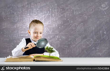 School education. Schoolgirl examining opened book with magnifying glass