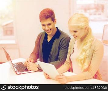 school, education, technology and internet concept - two teens with laptop and tablet pc at school