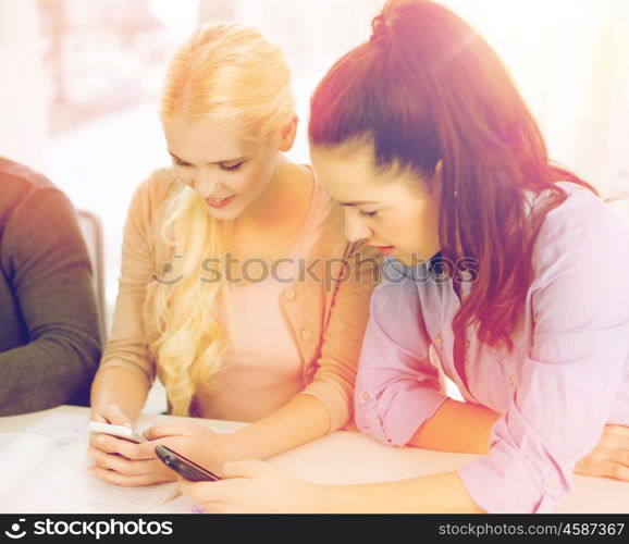 school, education, technology and internet concept - two teens with smartphones at school