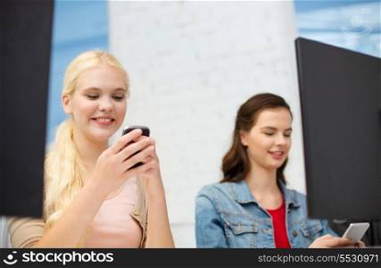 school, education, technology and internet concept - two teens with smartphones in computer class at school