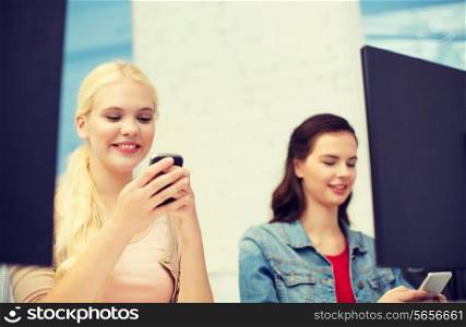 school, education, technology and internet concept - two teens with smartphones in computer class at school