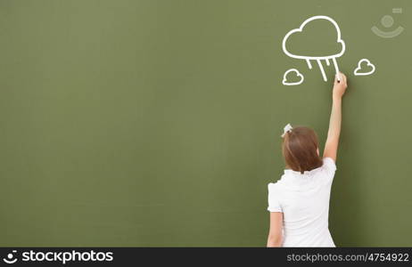 School girl at blackboard. Cute little girl standing with back and drawing on blackboard