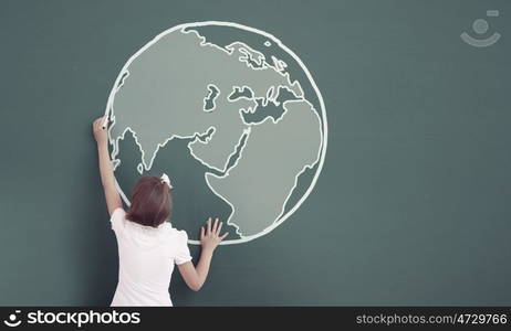 School girl at blackboard. Cute little girl standing with back and drawing planet on blackboard