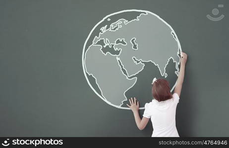 School girl at blackboard. Cute little girl standing with back and drawing planet on blackboard