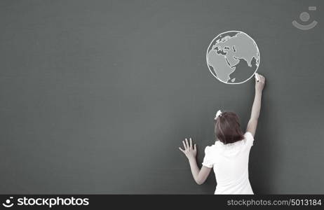 School girl at blackboard. Cute little girl standing with back and drawing planet on blackboard