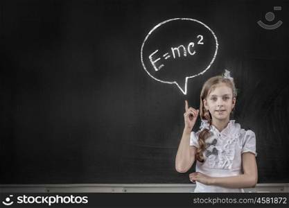 School girl at blackboard pointing at science formula with finger. Physics formula