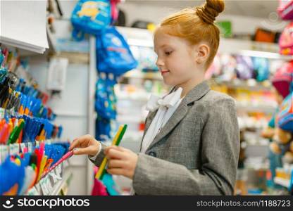 School girl choosing a pen at the shelf in stationery store. Female child buying office supplies in shop, schoolchild in supermarket. School girl choosing a pen in stationery store