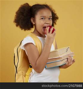 school girl eating apple holding books