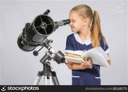 School girl looking through a telescope standing with textbooks
