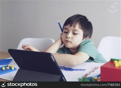 School kid in self isolation using tablet for homework,Child sad face lying head down looking out deep in thought, Boy stay at home during covid-19 lock down,Social Distance learning online education