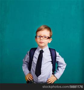School, kid, rucksack. little Boy in eyeglasses. Cheerful smiling little kid with big backpack against chalkboard. Looking at camera. School concept. Back to School