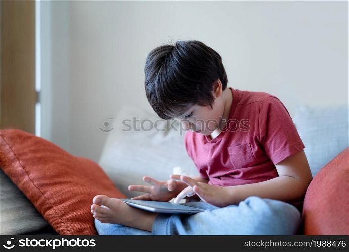 School kid sitting on sofa watching cartoon on tablet, Cute young boy playing game online on digital pad, Cinematic indoor portrait Child having fun and relaxing on his own in study room, Children with technology life style