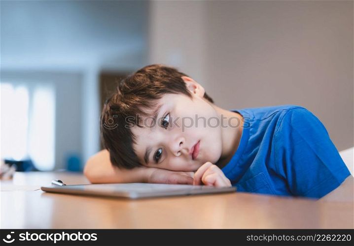 School kid using tablet for homework, Child bored face lying head down looking out deep in thought, Boy learning online class room at home, E-learning or Homeschooling education concept