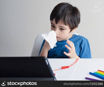 School kid wiping nose with tissue and watching cartoon on tablet,Child stay at home during corona virus home quarantine,E-learning, Home schooling ,Protective measures against spreading of Covid-19