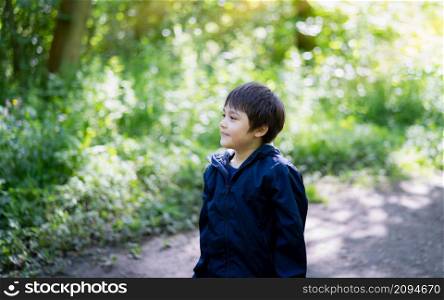 School kid with smiling face walking alone on in the garden, Cute Child playing outdoor with blurry green nature in the park,Portrait Young boy looking out deep in thought