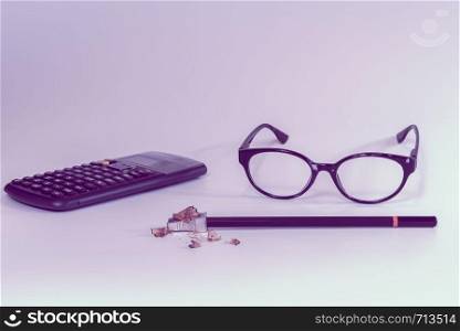 School or office supplies on a desk in feminine pink color with calculator, glasses, pencil and sharpener with wood shavings from sharpening - Concept of back to school, homework, learning or studying.. School or office supplies on a desk in feminine pink color with calculator, glasses, pencil and sharpener with wood shavings from sharpening - Concept of back to school, homework, learning or studying