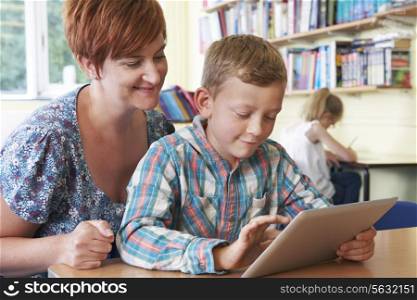 School Pupil With Teacher Using Digital Tablet In Classroom