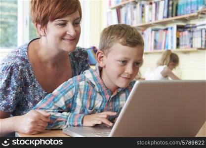 School Pupil With Teacher Using Laptop Computer In Classroom