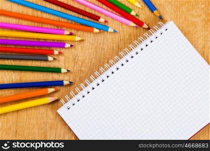 School stationary. Colored pencils and notepad on wooden table
