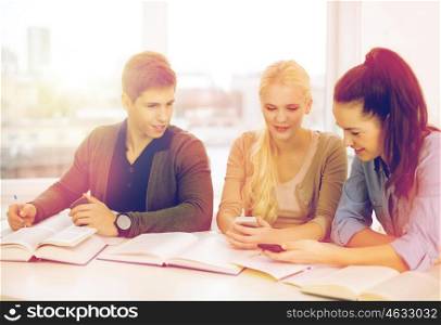 school, technology, internet and education concept - group of smiling students with smartphones and notebooks at school