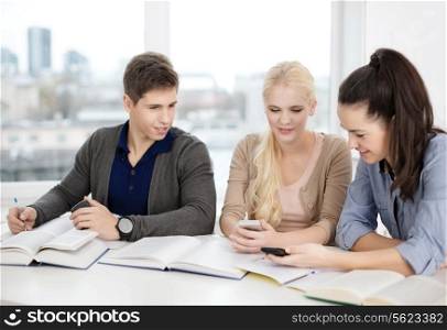 school, technology, internet and education concept - group of smiling students with smartphones and notebooks at school