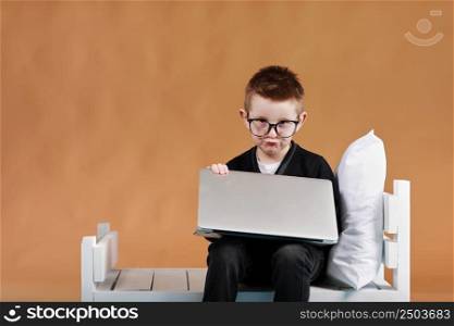 schoolboy in glasses closing laptop sitting on bed. Child doing school homework and tired looking on camera. Online learning, distance lesson, education with online tutor at home isolation.. schoolboy in glasses closing laptop sitting on bed. Child doing school homework and tired looking on camera. Online learning, distance lesson, education with online tutor at home isolation