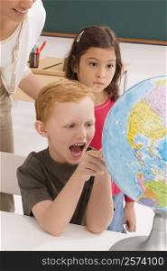 Schoolboy looking at a globe and shouting with a schoolgirl and a female teacher standing behind him