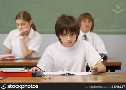 Schoolboy sitting at a desk with other students in the background