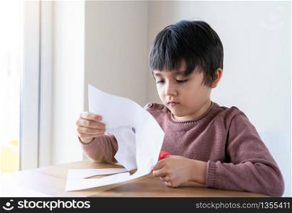 Schoolboy use scissors cutting shape of fish for homeworkKid learning how tocut paper, Child stay at home enjoys Arts and crafts activity during covid-19 lockdown, Home shoolling or Play and learn