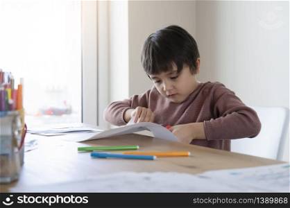 Schoolboy use scissors cutting shape of fish for homeworkKid learning how tocut paper, Child stay at home enjoys Arts and crafts activity during covid-19 lockdown, Home shoolling or Play and learn
