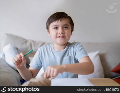 Schoolboy using green colour pen drawing on white paper sheet, Young kid doing school homework, Happy mixed race child enjoy doing arts and playing with toys, Home Education