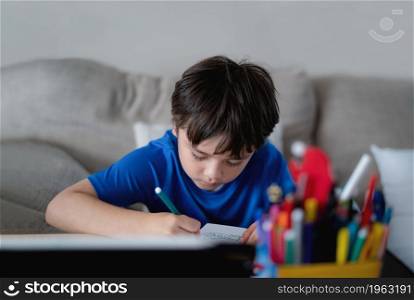 Schoolboy using green colour pen drawing on white paper sheet, Young kid doing school homework, Happy child enjoy doing arts and crafts at home on weekend. Home Education