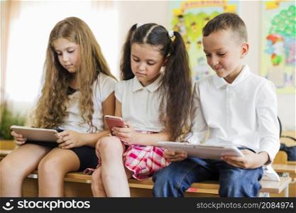 schoolchildren sitting bench holding gadgets