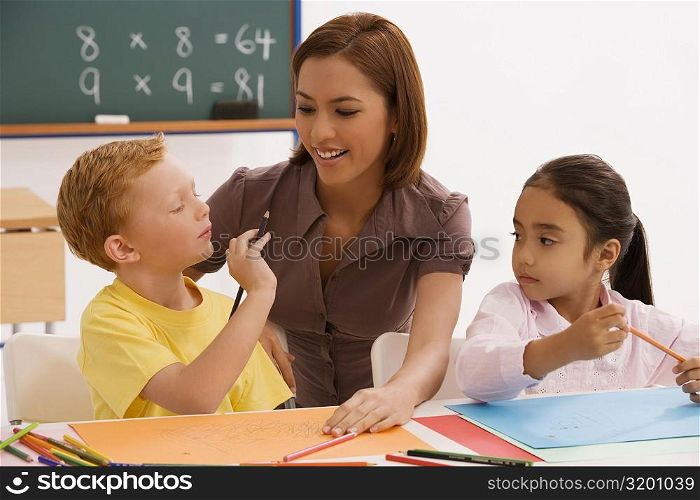 Schoolgirl and a schoolboy with their female teacher sitting in a classroom