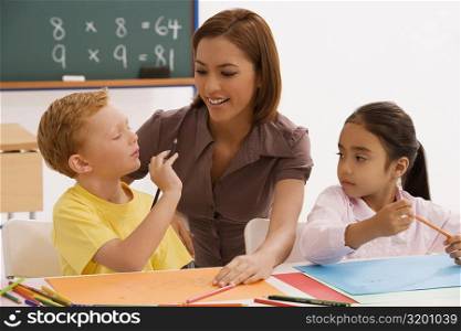 Schoolgirl and a schoolboy with their female teacher sitting in a classroom