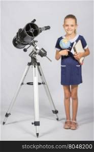 Schoolgirl astronomer is a telescope with a globe and books in the hands