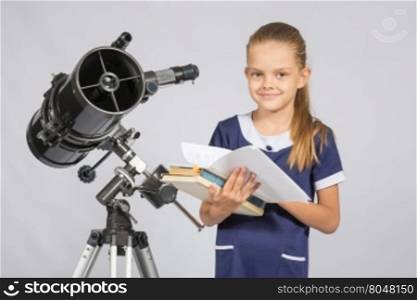 Schoolgirl astronomer leafing through books standing at the telescope