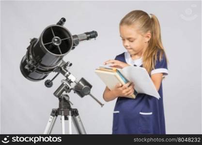 Schoolgirl astronomer leafing through books to find the right information at the stand of the telescope