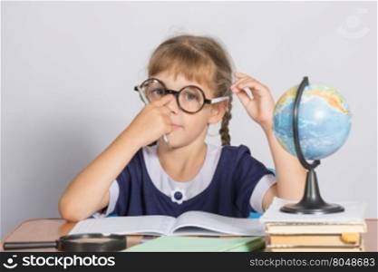 Schoolgirl corrects glasses while sitting at a desk in the classroom Geography