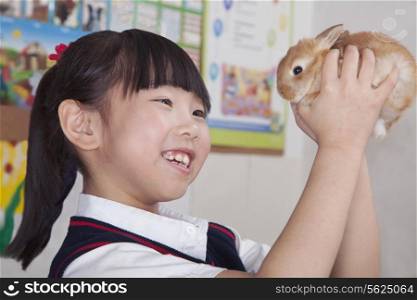 Schoolgirl holding pet rabbit in classroom